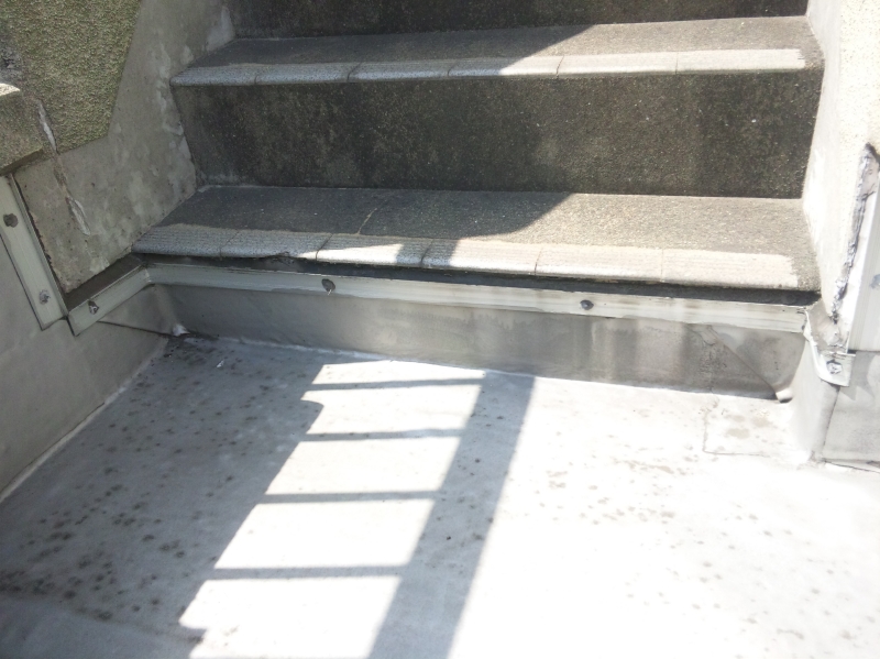 屋上床面からエレベーター機械室への階段。ゴムシート防水が１段目の蹴込みにかかっている。