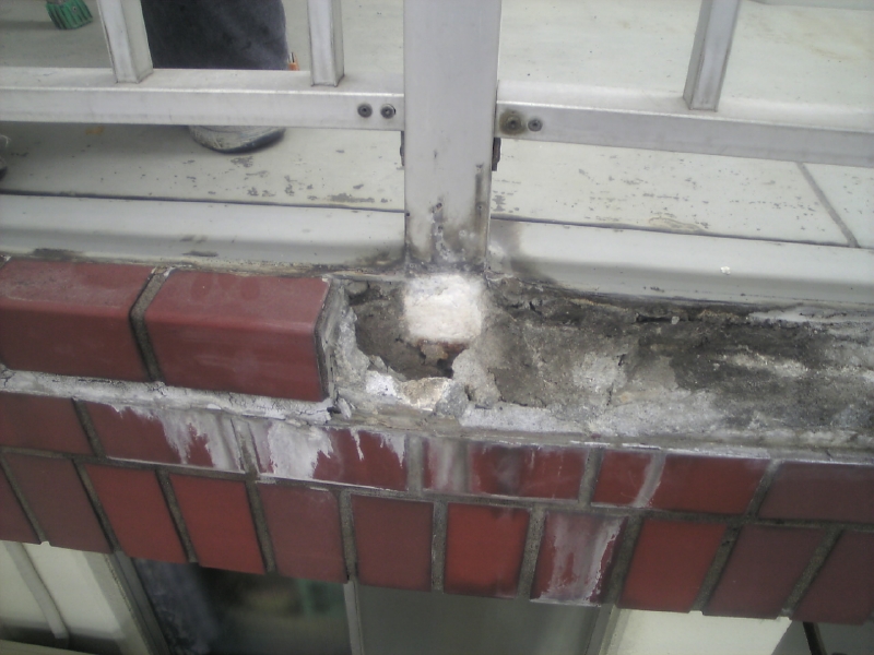 バルコニーのアルミ手摺足元。コンクリートが割れて内部が濡れていて、アルミ手摺の内部に埋まっている支柱の腐食が顕著。