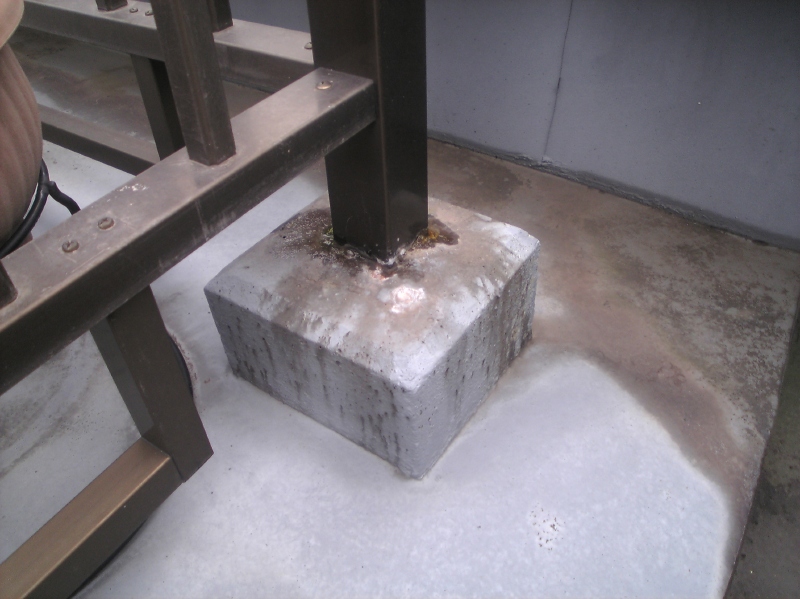 ルーフバルコニーのアルミ手摺支柱。モルタルとの取り合いの足元が濡れてコケも生えている。